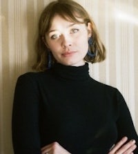 a woman in a black turtleneck shirt leaning against a wall