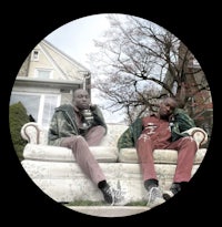 two men sitting on a couch in front of a house